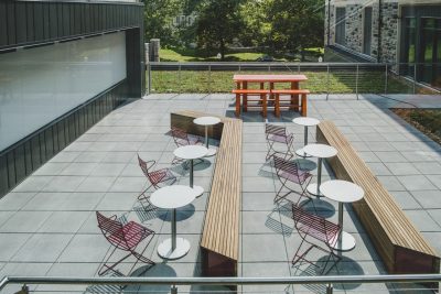 Outdoor classroom area with large whiteboard and white bistro tables and maroon chairs