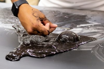 A student holds a magnetic over a large, black bubble that is coming out of the magnetic slime.