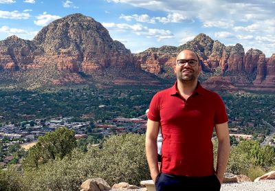 Abdelaziz Alsharawy, lead author on the study and a recent Ph.D. graduate in economics, stands in front of a large mountain range in Arizona. Above the range, clouds dot the bright blue sky.