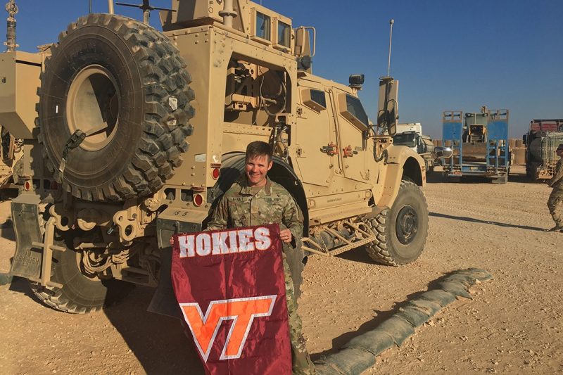 Maj. Ryan Strait holds a Virginia Tech flag in front of an Army vehicle.