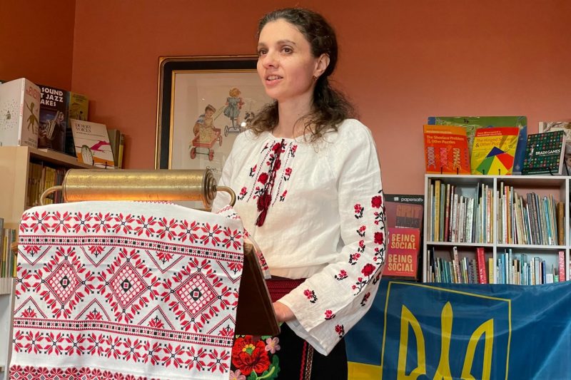 Kira Gulko Morse stands at a podium. She wears a traditional Ukrainian shirt.