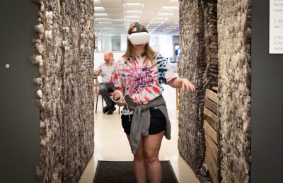 A female student walks through the exhibit wearing virtual reality gear.
