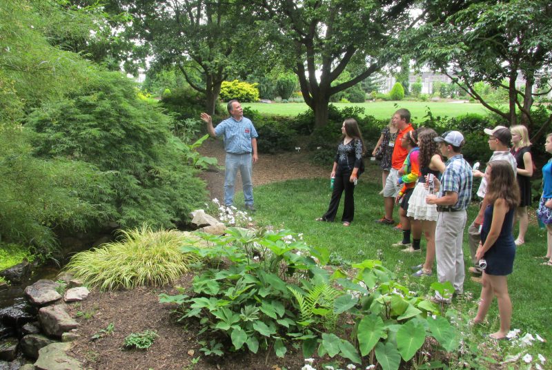 A man stands in front of a group of students in a garden.