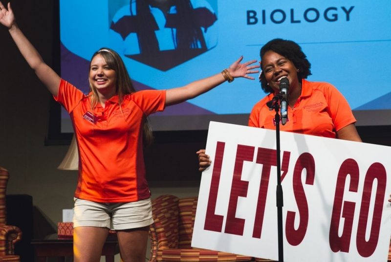 Ariana Mollers stands on stage at orientation beside a fellow leader holding a "Let's Go" sign