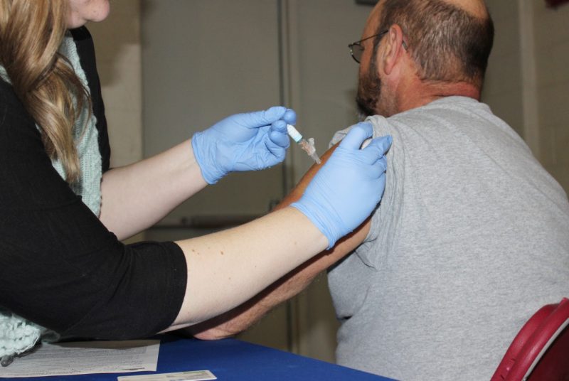 An employee receives a flu shot in his arm.