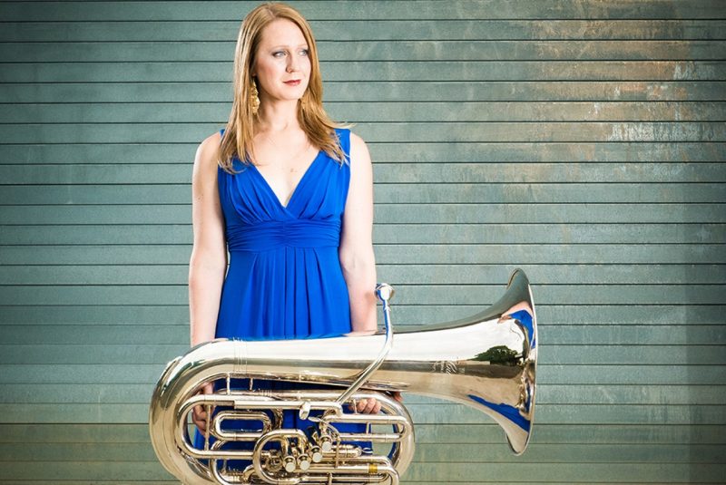 Carol Jentsch stands holding her tuba, dressed in a blue gown.