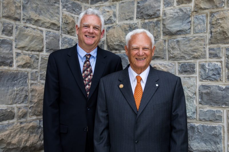 In the posed photo, father and son smile for the camera in front of a Hokie stone background.
