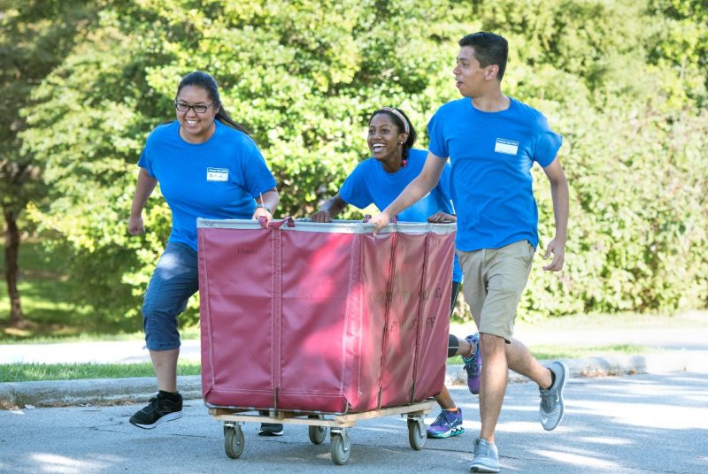 three students run with a rolling laundry cart to help Hokies move in to residence halls