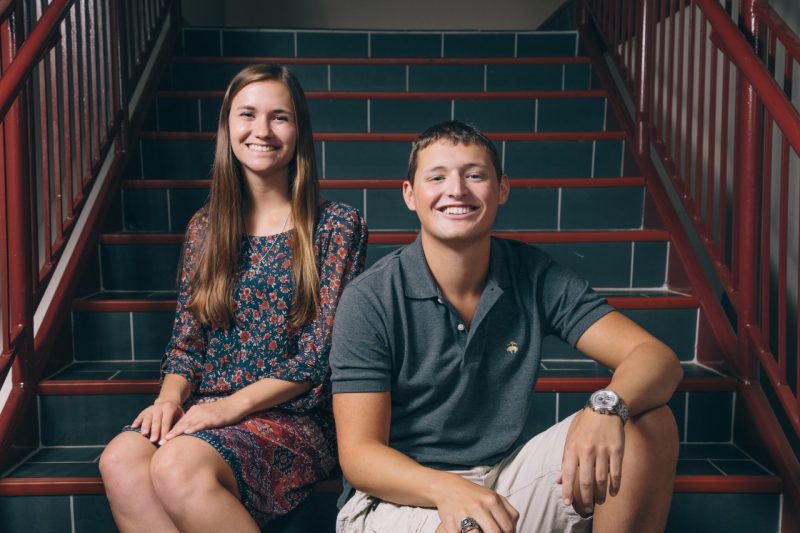 Allison Teresa Burns and Cameron Myers sit beside one another on a staircase.