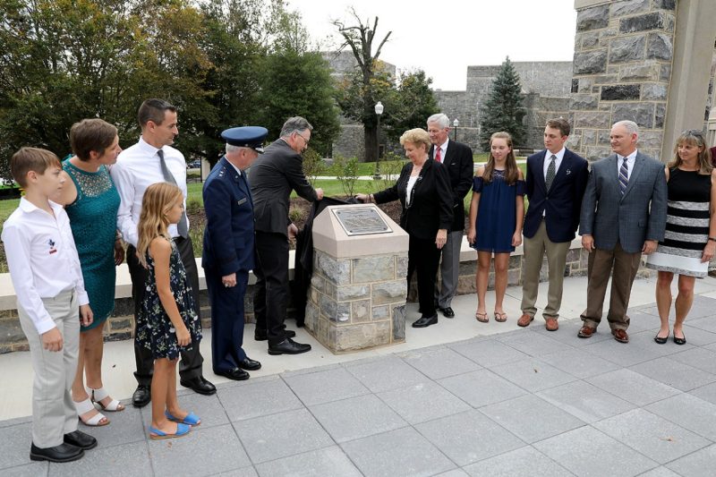 President Tim Sands and Georgia Anne Snyder-Falkinham pull back a black cloth to unveil the marker for the Peter Caldwell Snyder Flagpole Plaza.