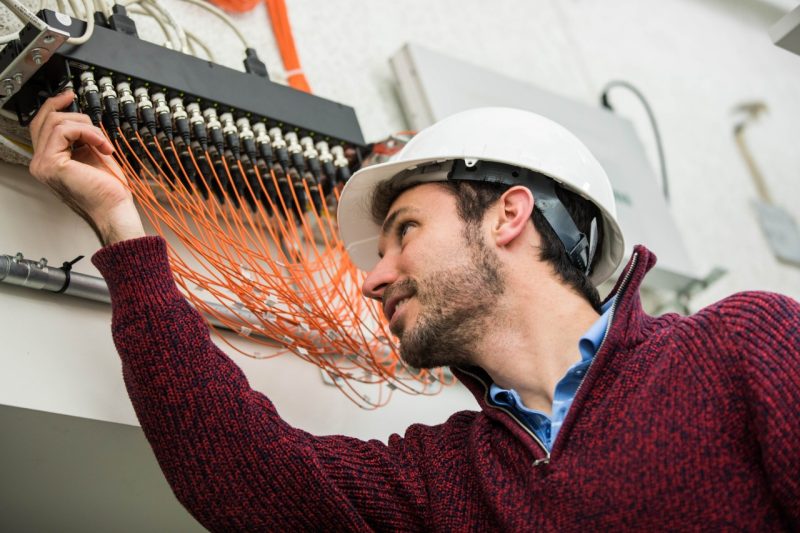 Photo of a man, Rodrigo Sarlo, reaching up toward orange wires connected to a boxy server system.