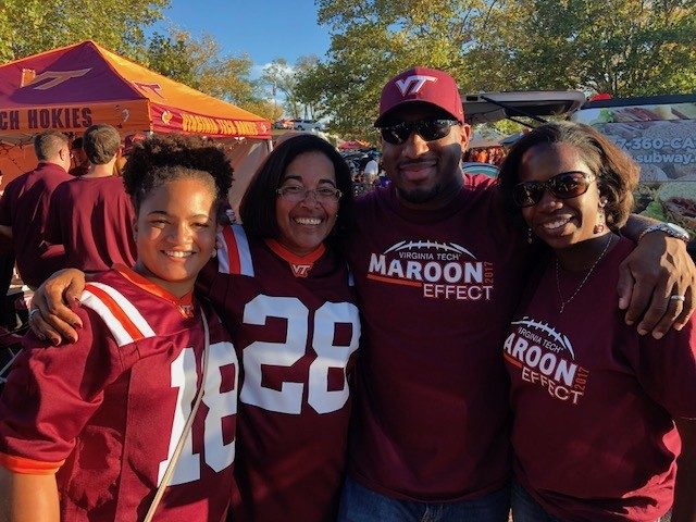 Four people pose for a photo on a game day, wearing Hokies jerseys and maroon and orange.