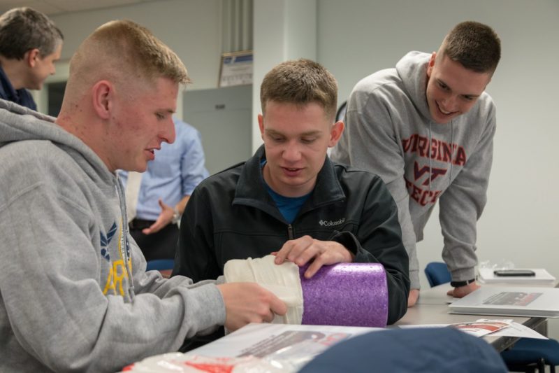 Three male students practice wrapping a wound