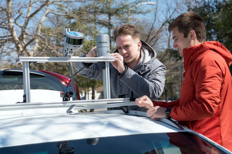 Two students tweak a small circular sensor on the top of a white car.