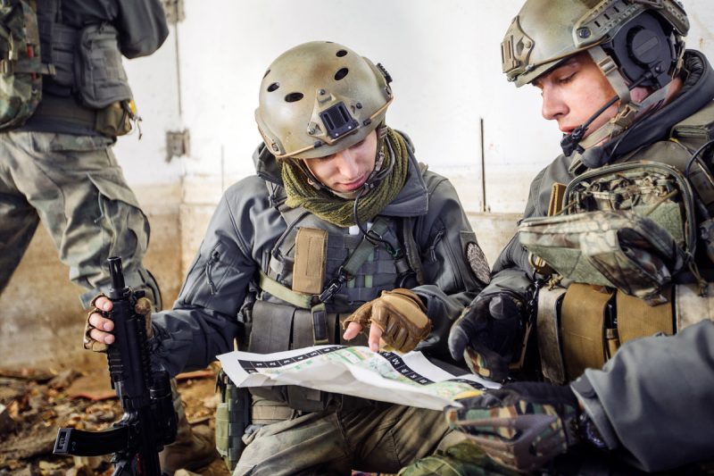 Soldiers disucss plans together while kneeling on the ground.