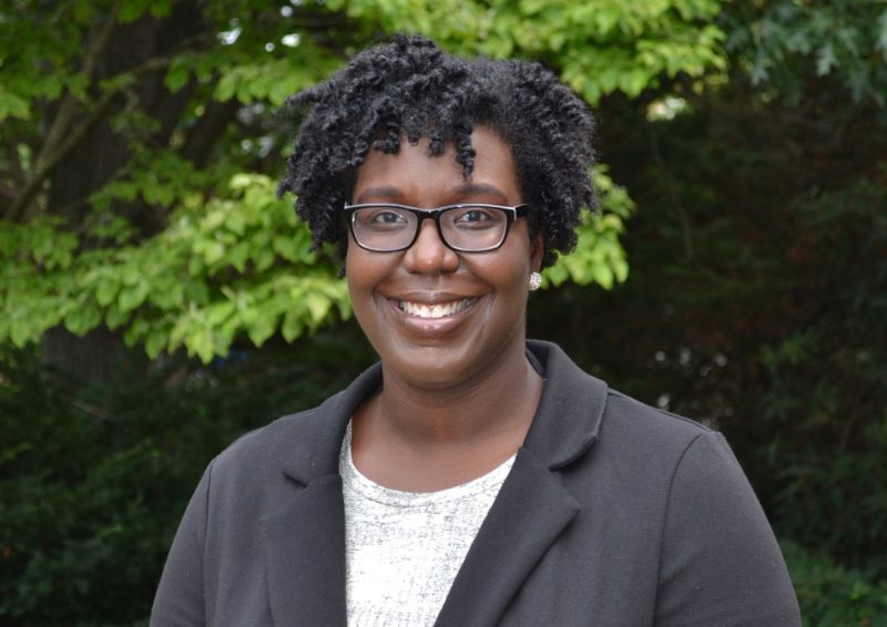 Profile photo of Shernita Lee wearing a white shirt, gray jacket and glasses, smiling in front of trees outside the Graduate Life Center. She is the Director of the Graduate School's Office of Recruitment, Diversity, and Inclusion