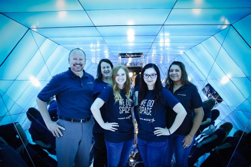 Five of Lockheed Martin's staff members stand smiling inside of the challenge box, which is completely covered with mirrors. 