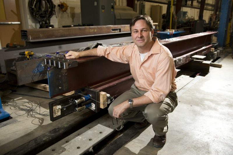 A photo of a man posing next to structural engineering test equipment.