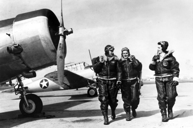 Three Women Airforce Service Pilots walk on an airfield during World War I.