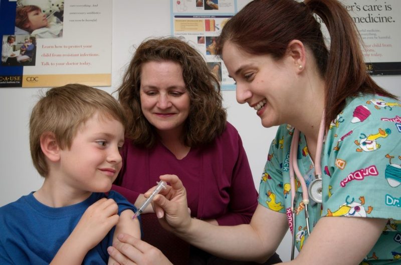 A nurse administers an intramuscular vaccination to a young boy with his mother looking on.
