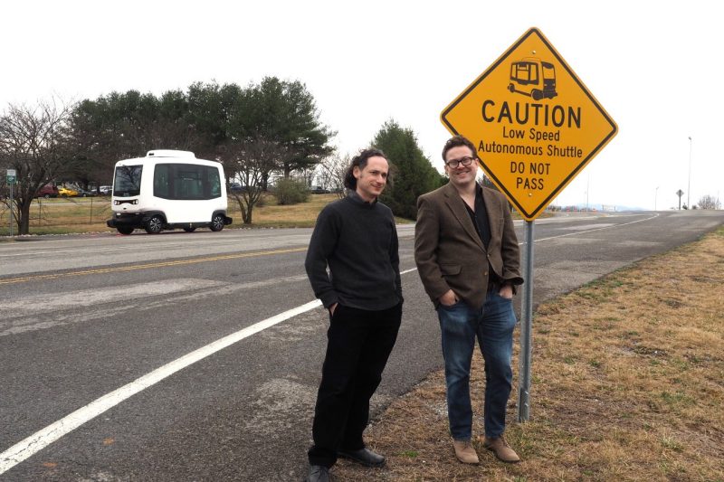 Saul Halfon (left) and Lee Vinsel stand in front of a sign that states, "Caution. Low Speed Autonomous Shuttle. Do Not Pass."