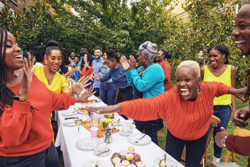Members of the Kingdom Choir sing around an outdoor dining table.
