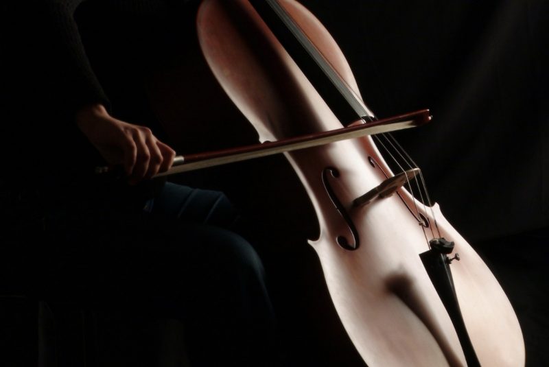 A hand holding a bow slides against the strings of a cello.