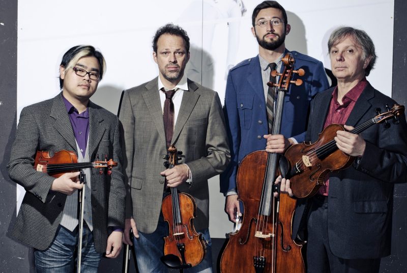 Members of the Sirius Quartet pose against a wall holding their instruments.