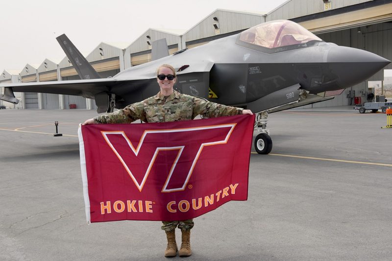 U.S. Air Force 1st Lt. Samantha Reed stands in front of an aircraft holding a Hokie flag.