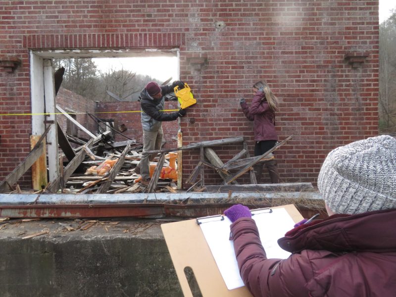 Students using measuring tools on abandoned brick building.