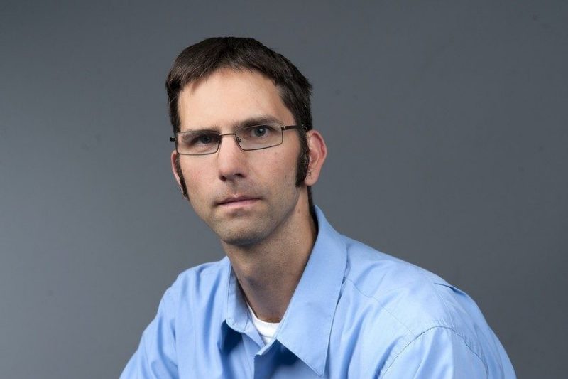 Jonathan Petters sitting in front of a gray background wearing a blue shirt. 