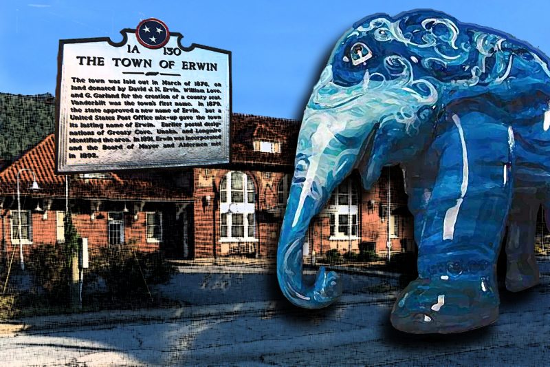 Blue elephant statue in foreground with town plaque and old depot in background