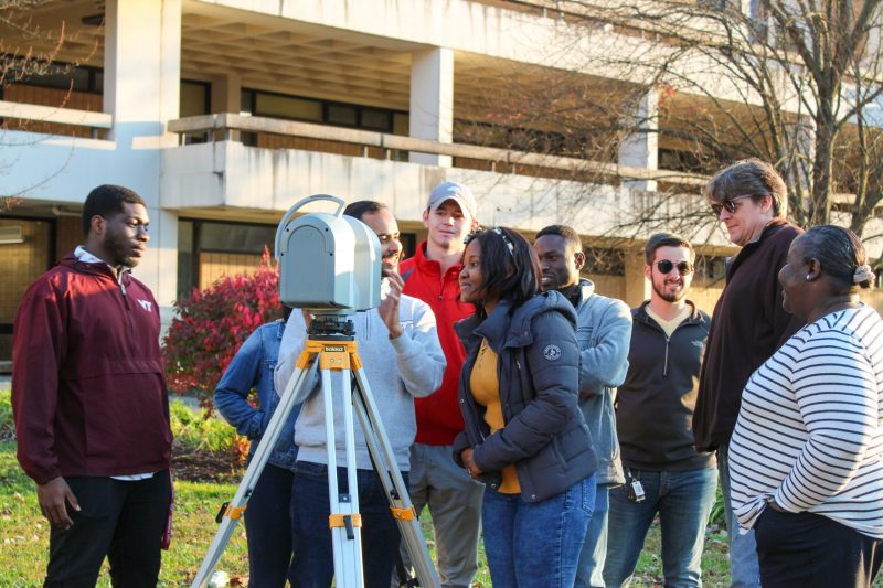 Students look at sensing equipment on a tripod at a campus location outdoors. 