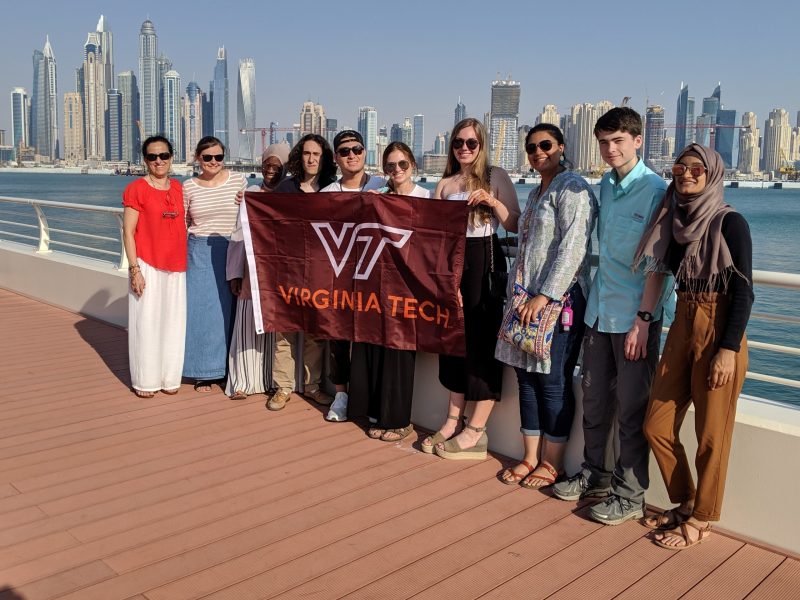Students participating in the Virginia Tech Arabic in Oman study abroad program hold up a Virginia Tech flag with Dubai as a backdrop. 
