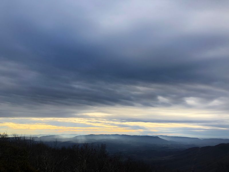 An image shows sun shining through the clouds onto the mountains from Bald Knob