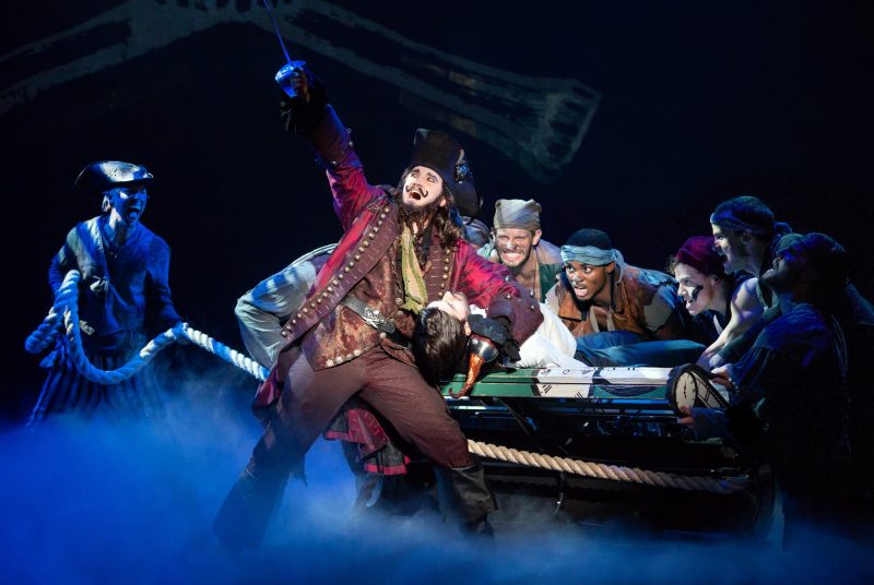 Captain Hook raises his hook to the sky while surrounded by other shady characters during an onstage scene of "Finding Neverland."