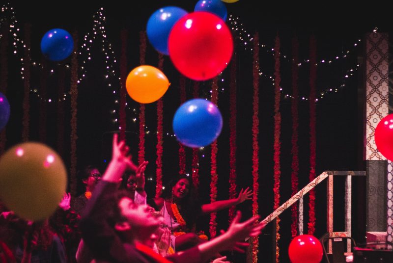 Audience members laugh and celebrate with colorful balloons onstage.