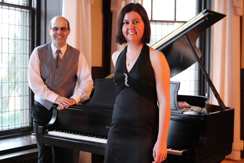 Canadian pianists Gregory Millar and Lisa Raposa, the Millar Duo, stand in front of a grand piano.