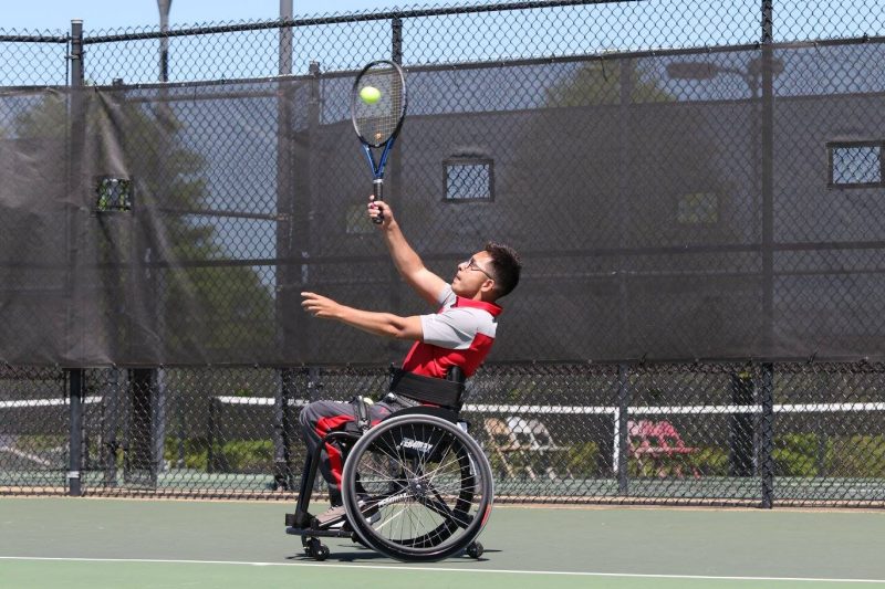 Player in wheelchair returns tennis ball 