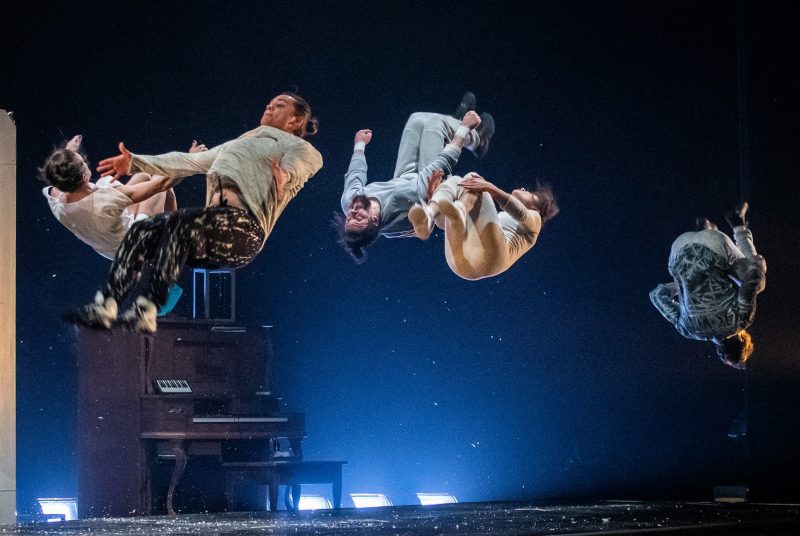 Five performers with cirque act Flip Fabrique are all suspended in the air, mid-backflip, while performing onstage.