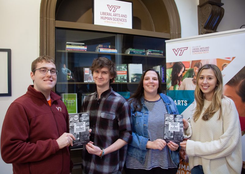 From left, Frank Powell, Seth Hendrickson, Kayla Mizelle, and Brianna Sclafani hold a copy of their book in front of a bookshelf in the Liberal Arts and Human Sciences building.