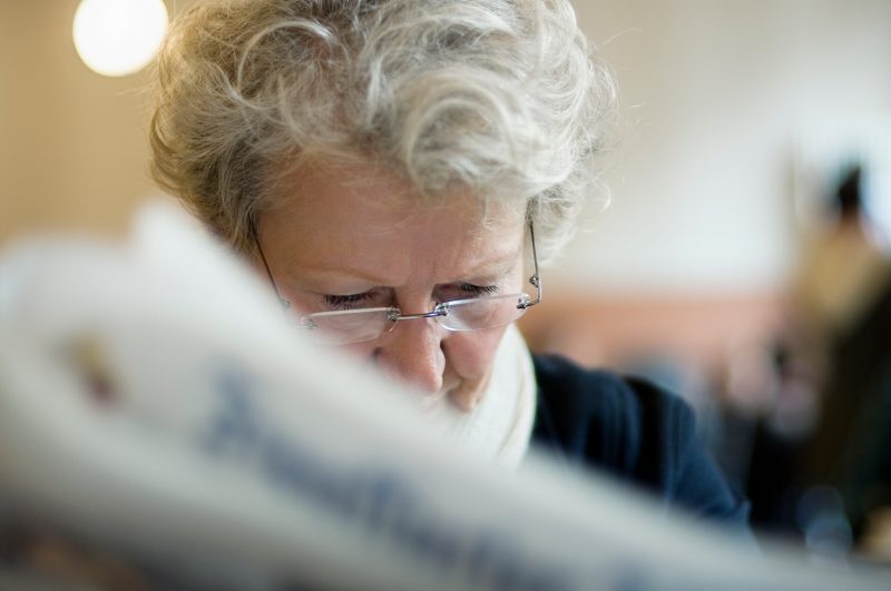 An older woman reads a newspaper.