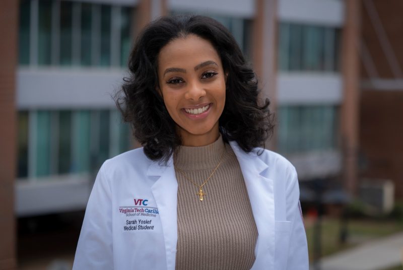 Female wearing medical white coat outside with building in background