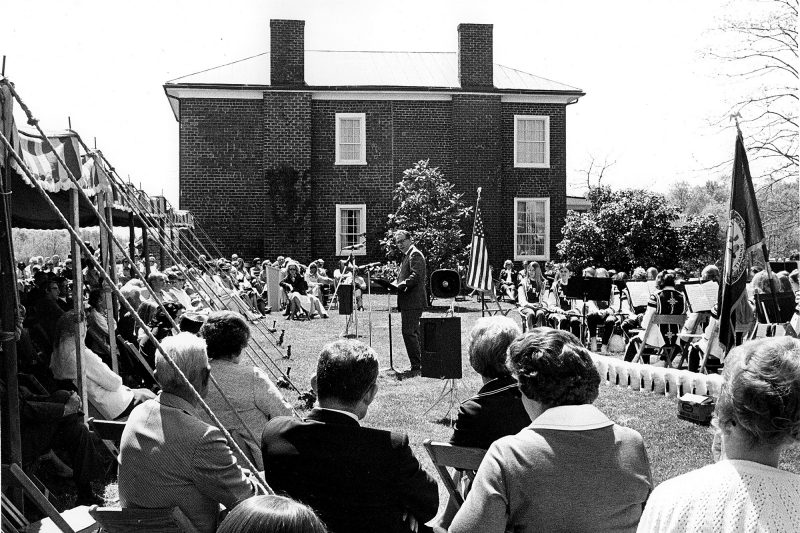 Black and white photo from 1970 dedication showing a crowd sitting in the lawn next to the historic home.