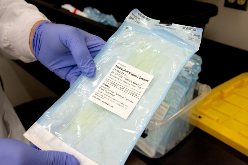 Marc Michel, out of frame except his hands, holds a bag of sterilized, inspected 3D-printed nasopharyngeal swabs. The bag is clear  with instructions printed on the front.  Michel is wearing gloves as he holds the bag.