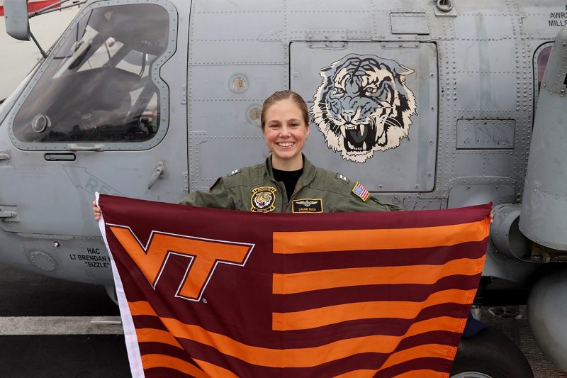 Lt. Cassandra Quick holds a Virginia Tech flag in front of a MH-60 Romeo.
