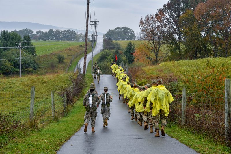 A line of cadets in yellow rain ponchos walks the rolling hills of a paved trail.