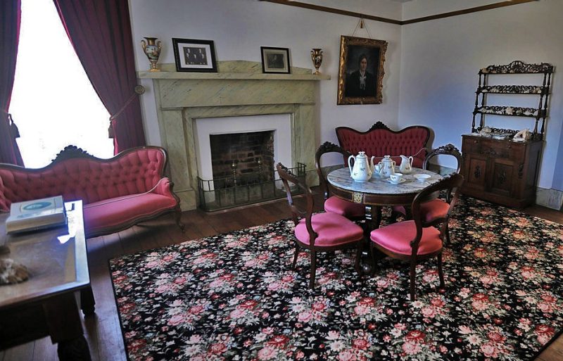 The parlor of the Reynolds homestead features a large fireplace and antique furniture with pink upholstery. 