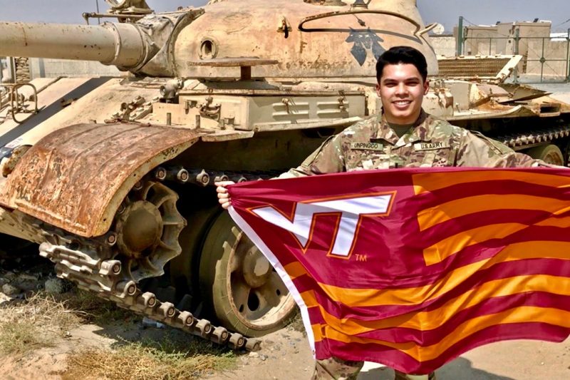 U.S. Army 1st Lt. Peter Unpingco holds a Virginia Tech flag in front of a tank while deployed to Afghanistan.