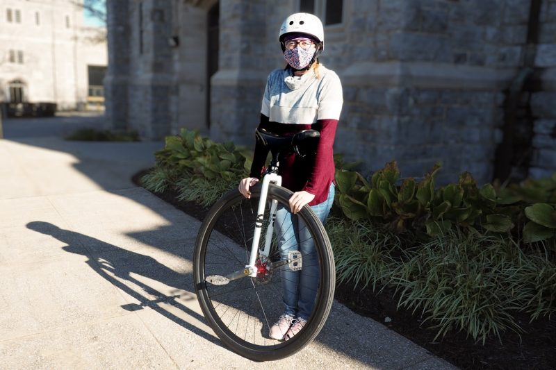Sabrina stands in front of a building with her unicycle